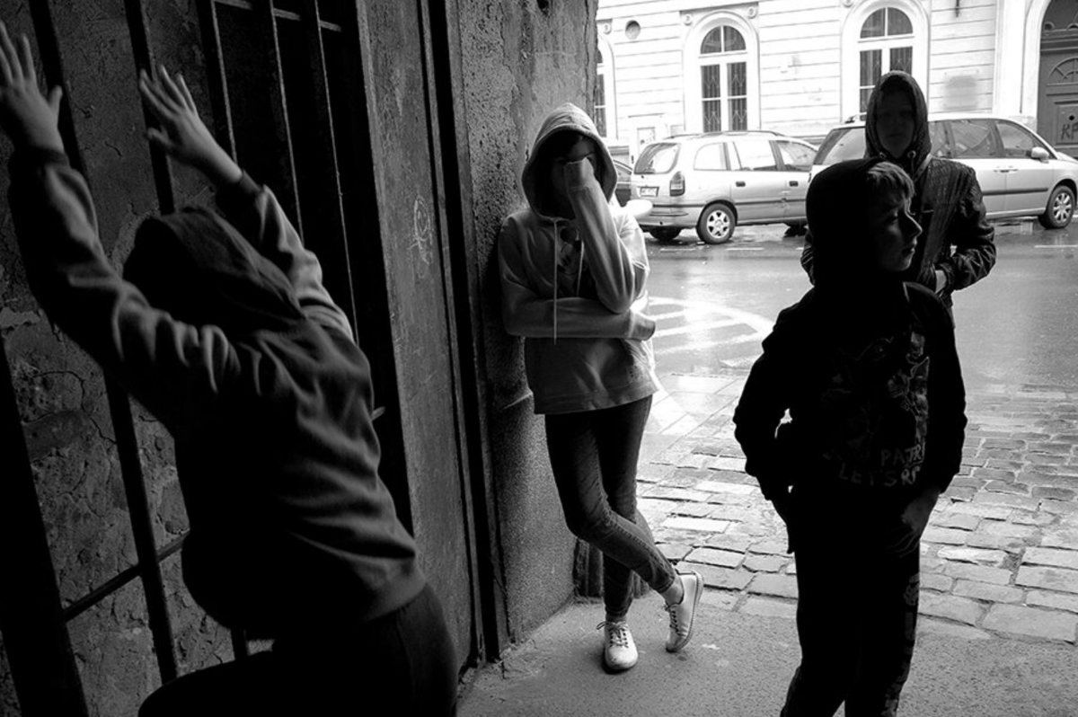 Czarno-białe zdjęcie czwórki dzieci, które stoją przy wejściu do kamienicy na mokrym bruku.
